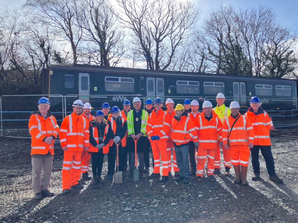 Stakeholders gather at site of Okehampton Interchange station, with train in background