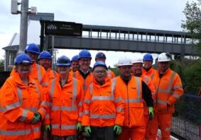 Partners in high vis jackets on the platform at Okehampton Interchange, with footbridge behind them